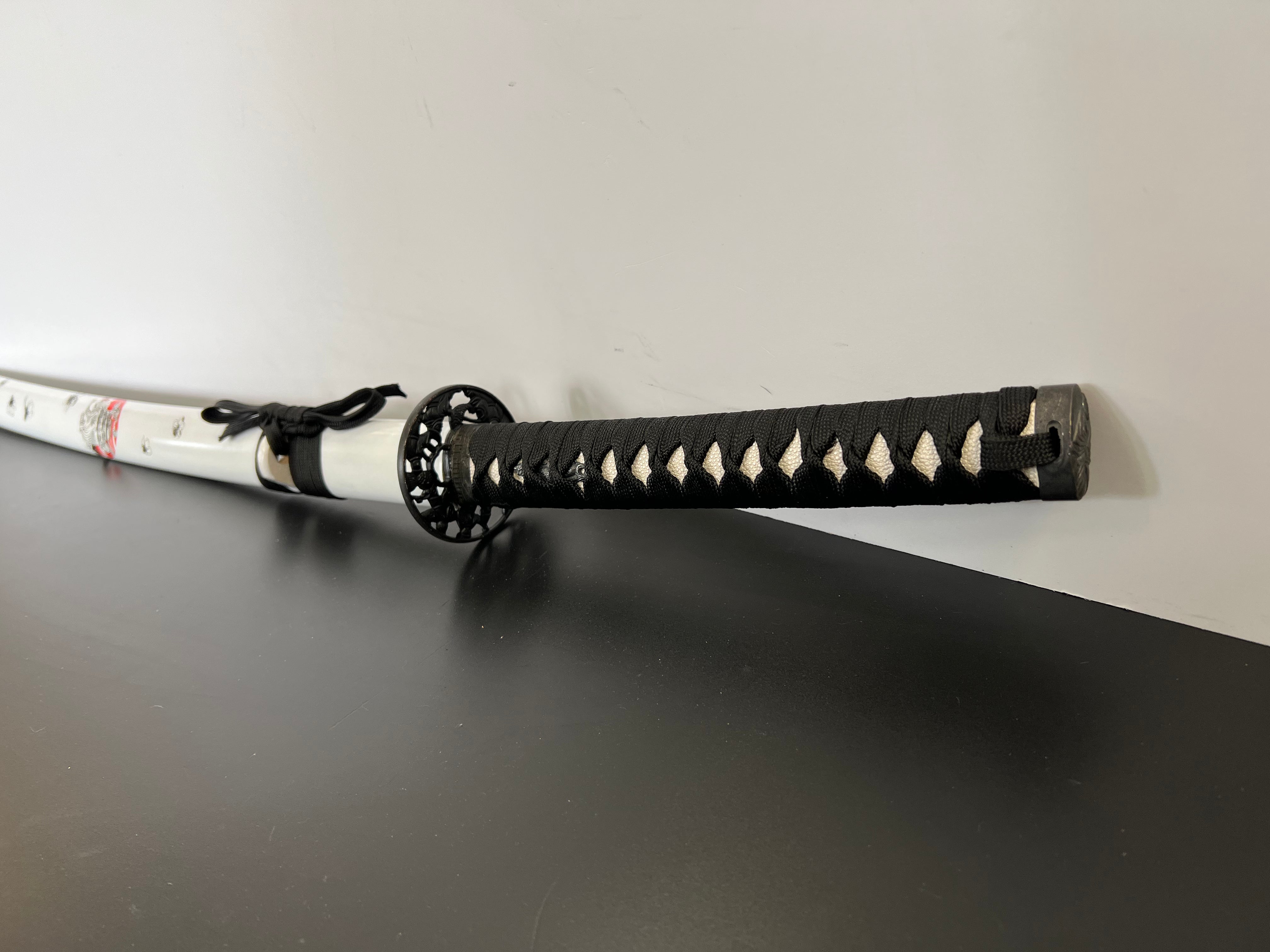 Katana mit weißen Kirschblütenmuster. Das Samuraischwert hat Kirschblüten Verzierungen auf der ganzen Saya (Schwertscheide) und die Kirschblüte ist eines der wichtigsten Symbole in Japan, sie steht für Schönheit, Aufbruch und Vergänglichkeit und zeigt sich in der schönsten Jahreszeit, dem Frühling.  Die Kirschblüte wird im Japanischen Sakura genannt und wird von vielen Japanern aufgrund ihrer Schönheit gepflanzt. Zudem spiegelt die Kombination aus Katana und Kirschblüte die Japanische sehr gut wieder.